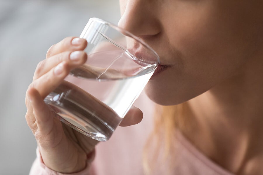 Una giovane donna beve un bicchiere d'acqua per contrastare la cellulite